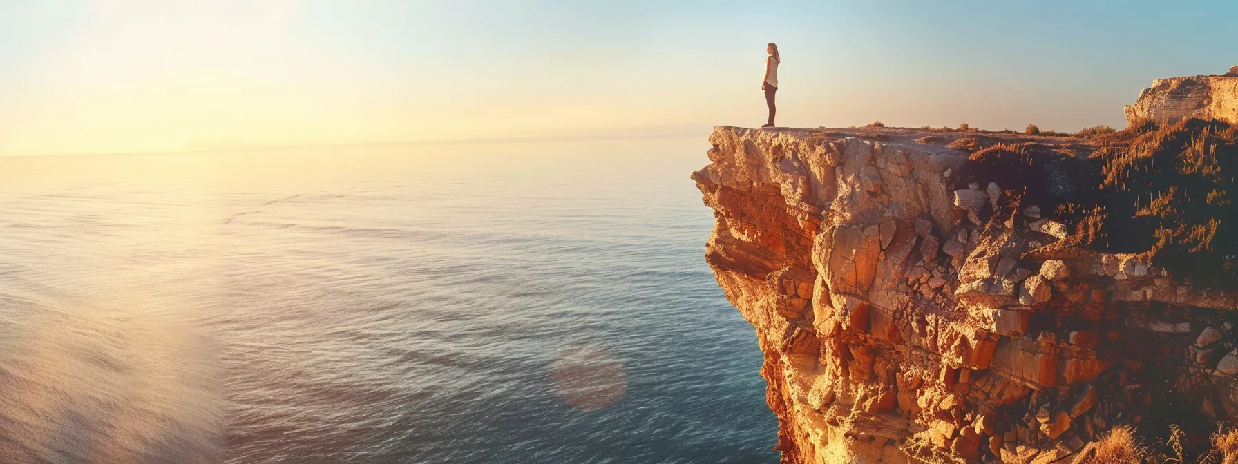 a person standing on the edge of a cliff overlooking a vast horizon with a clear sky, signifying infinite possibilities and a mindset ready for breakthrough success.