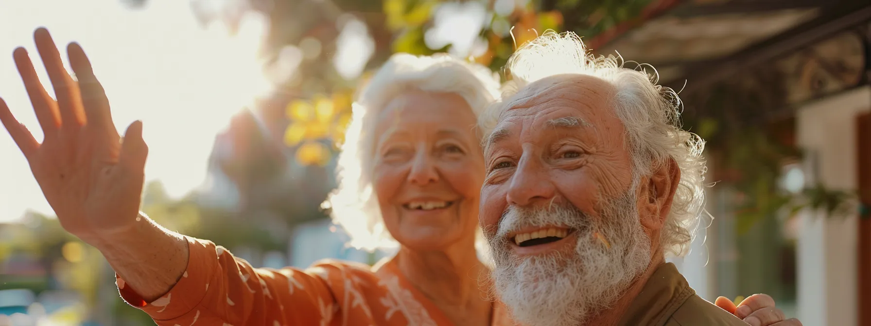 a senior couple smiling and waving at the camera while standing outside a geriatric practice.