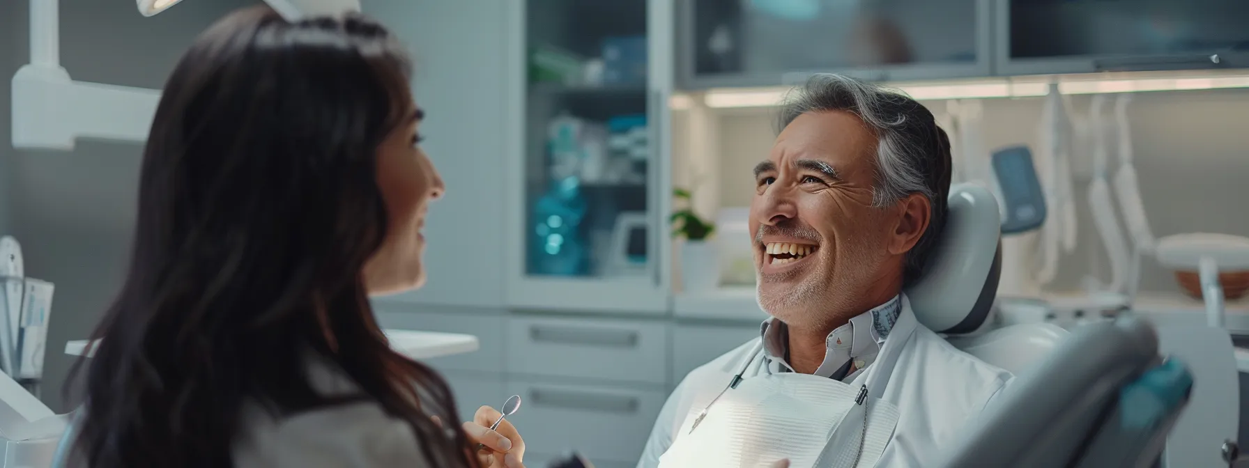 a dentist talking with a smiling patient in a treatment room.